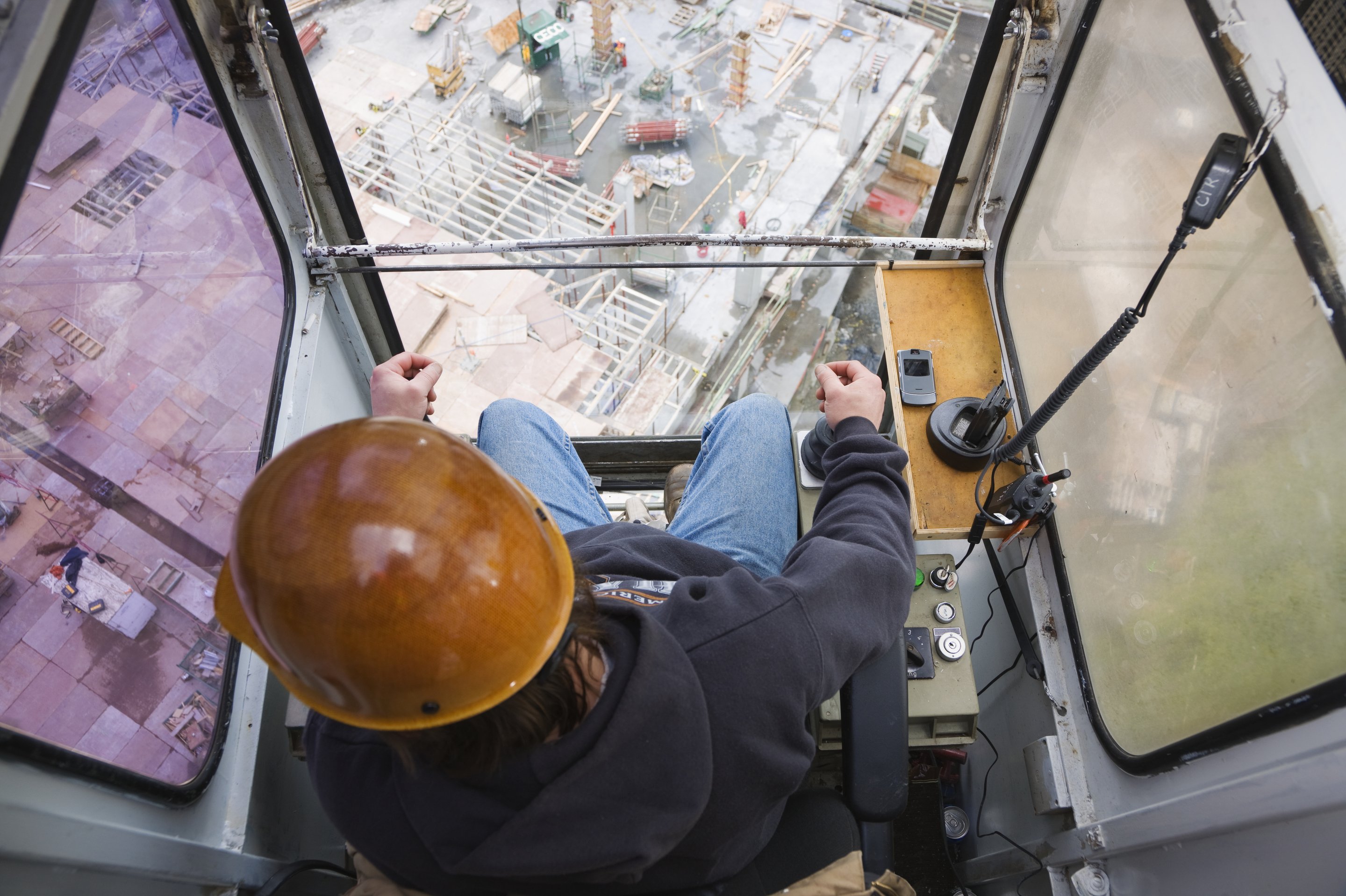 High-angle perspective of a crane operator sitting in a cab overlooking an active construction site.