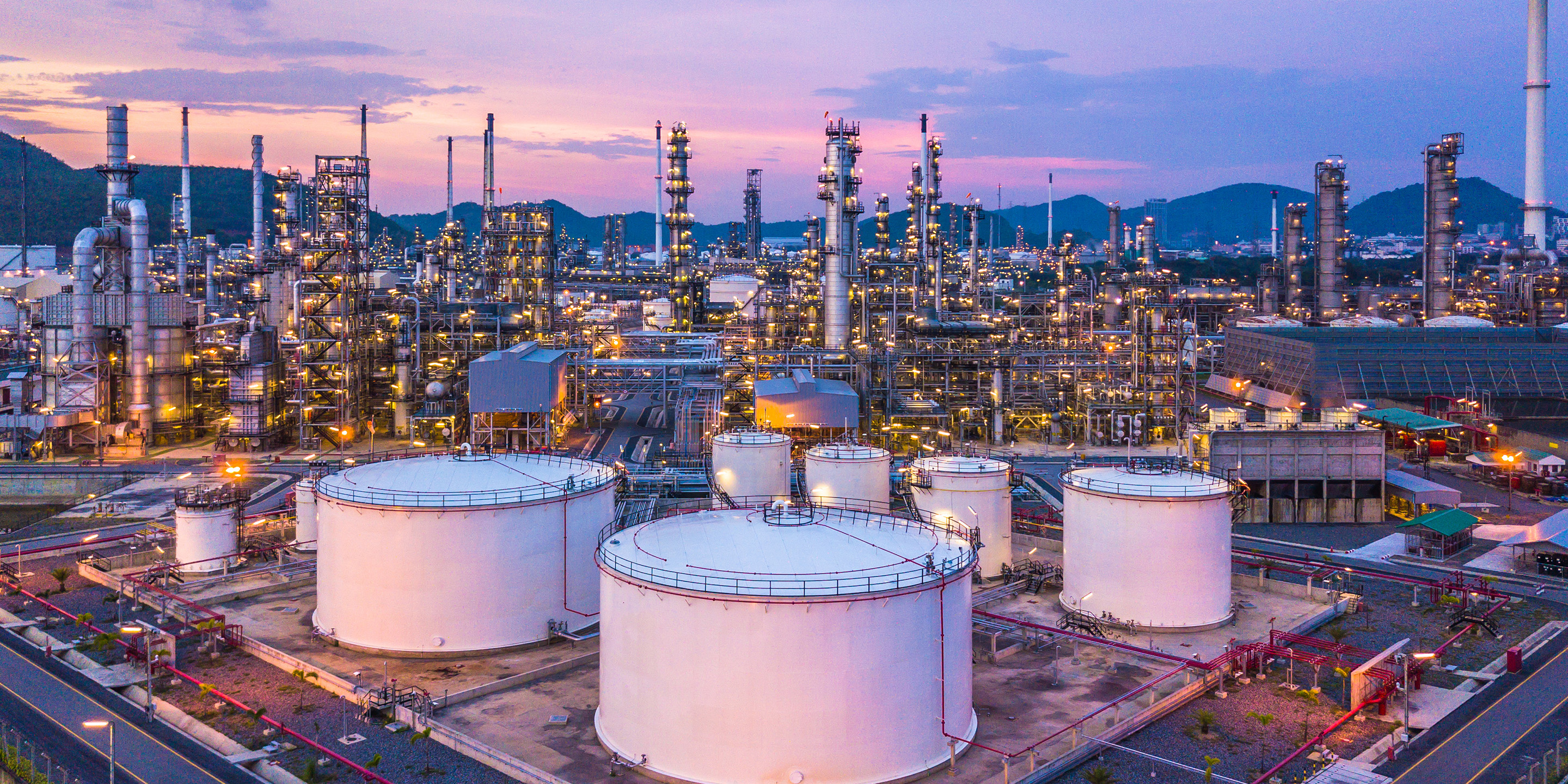 Stunning aerial image of an oil refinery during sunset, highlighting storage tanks, towers, and intricate industrial infrastructure.